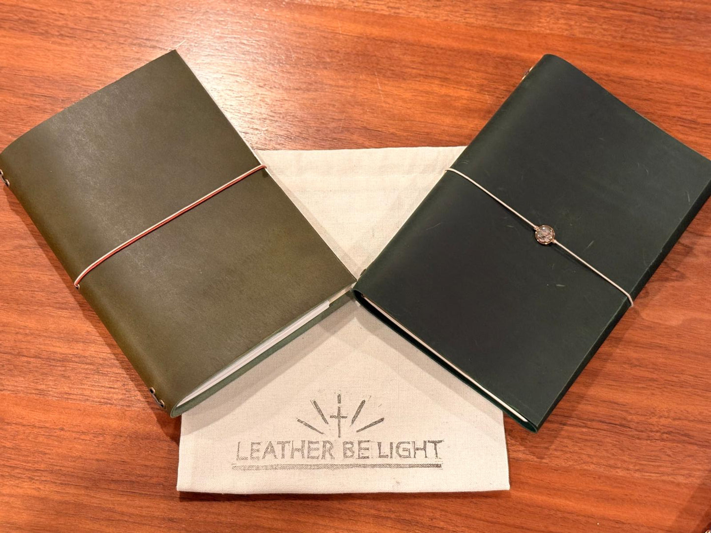 Two leather-bound notebooks on a wooden surface with 'Leather Be Light' branding.