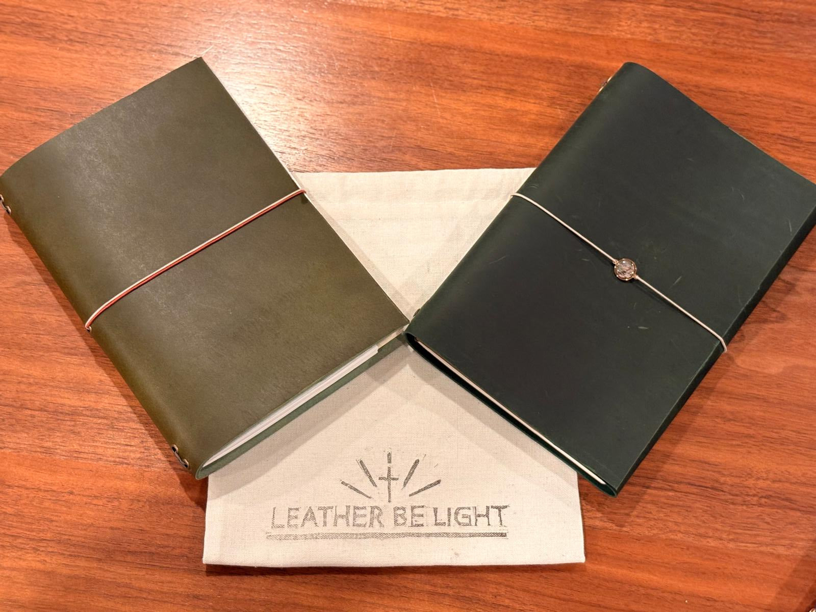 Two leather-bound notebooks on a wooden surface with 'Leather Be Light' branding.