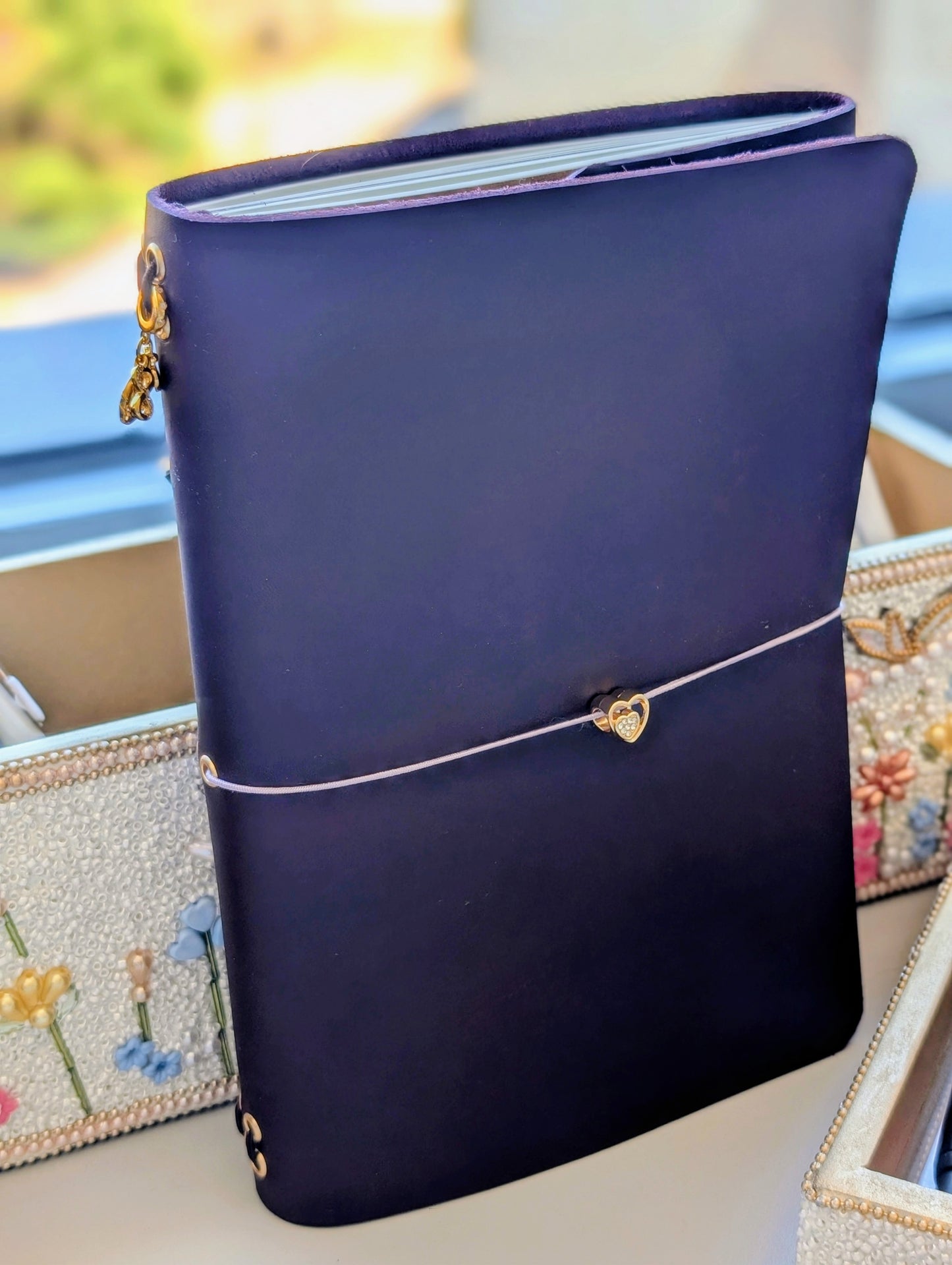 Blue-Violet notebook with an elastic closure and gold charms on a decorative surface