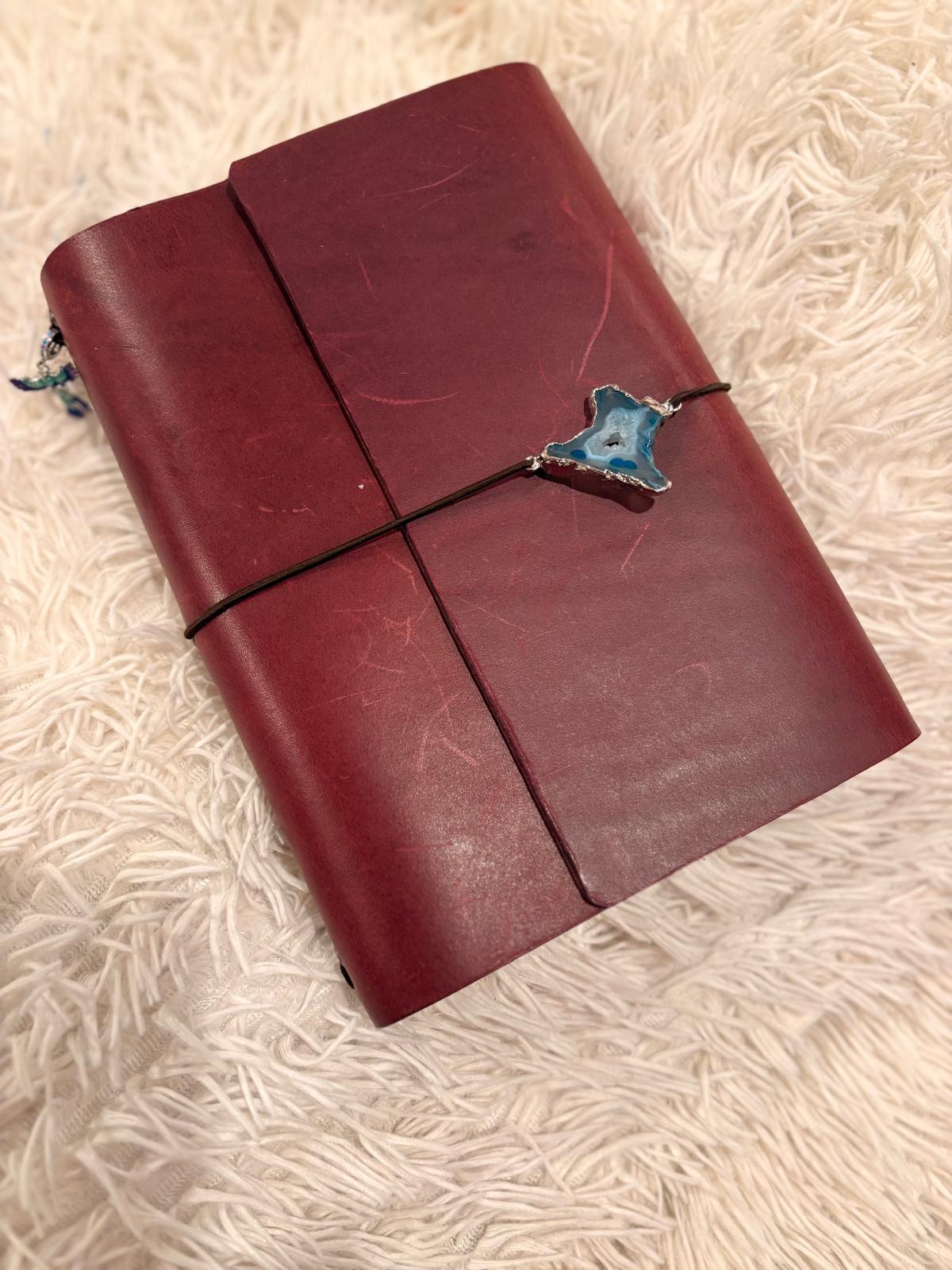 Violet leather notebook with a decorative geode clasp on a textured beige surface